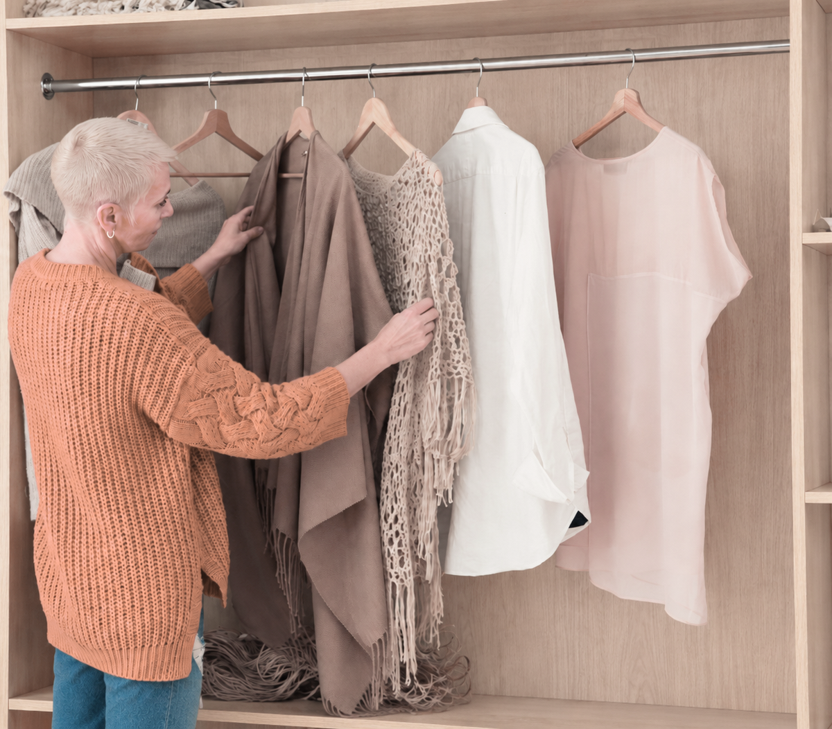 A woman choosing what to wear, one hand on a garment along the rail of her wardrobe. Image