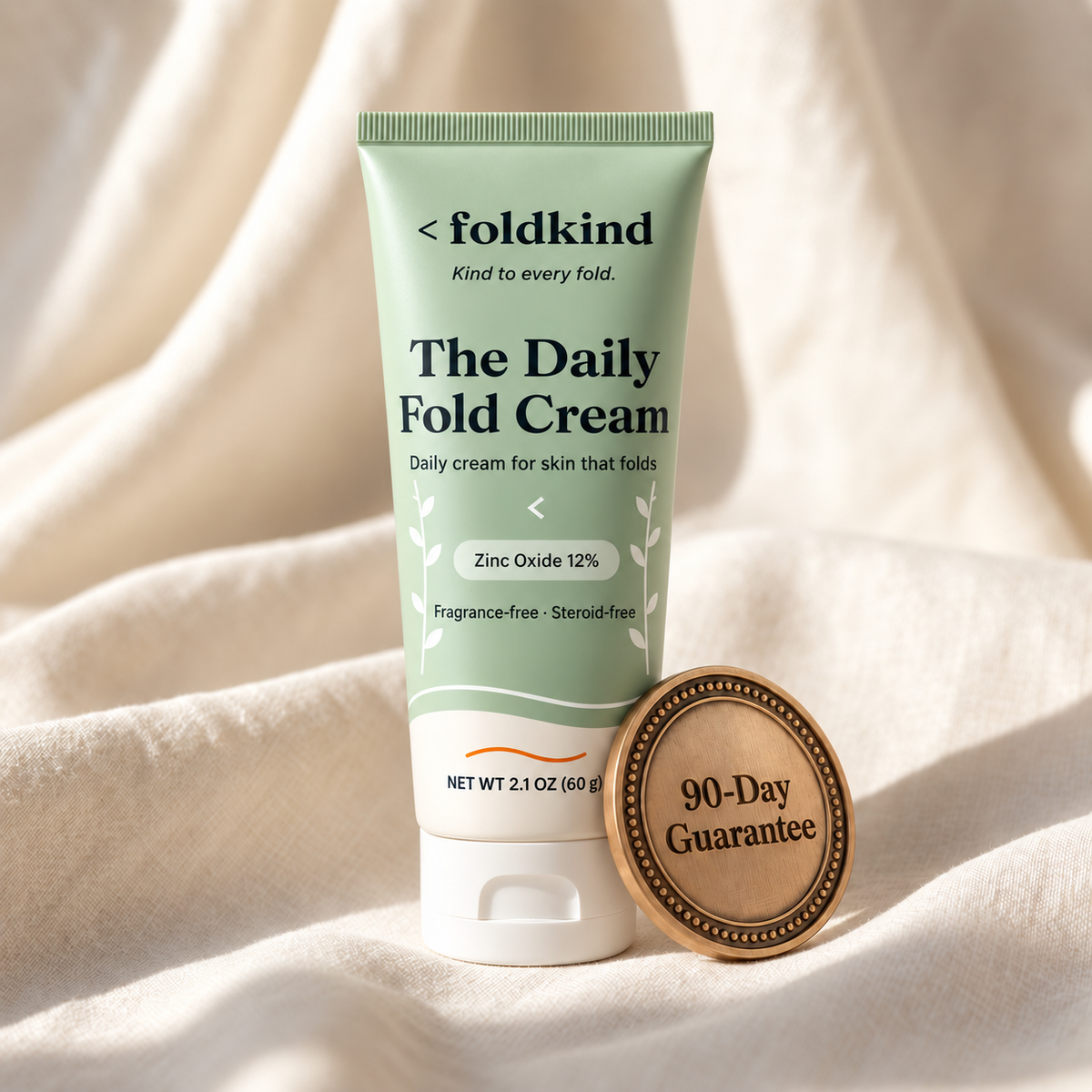 The Daily Fold Cream tube on ivory linen with a bronze 90-day guarantee medal resting against it. Image