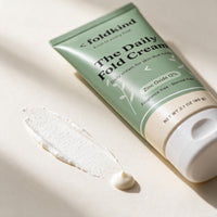 A thin smear of The Daily Fold Cream drying to a matte, powder-soft finish beside the tube.