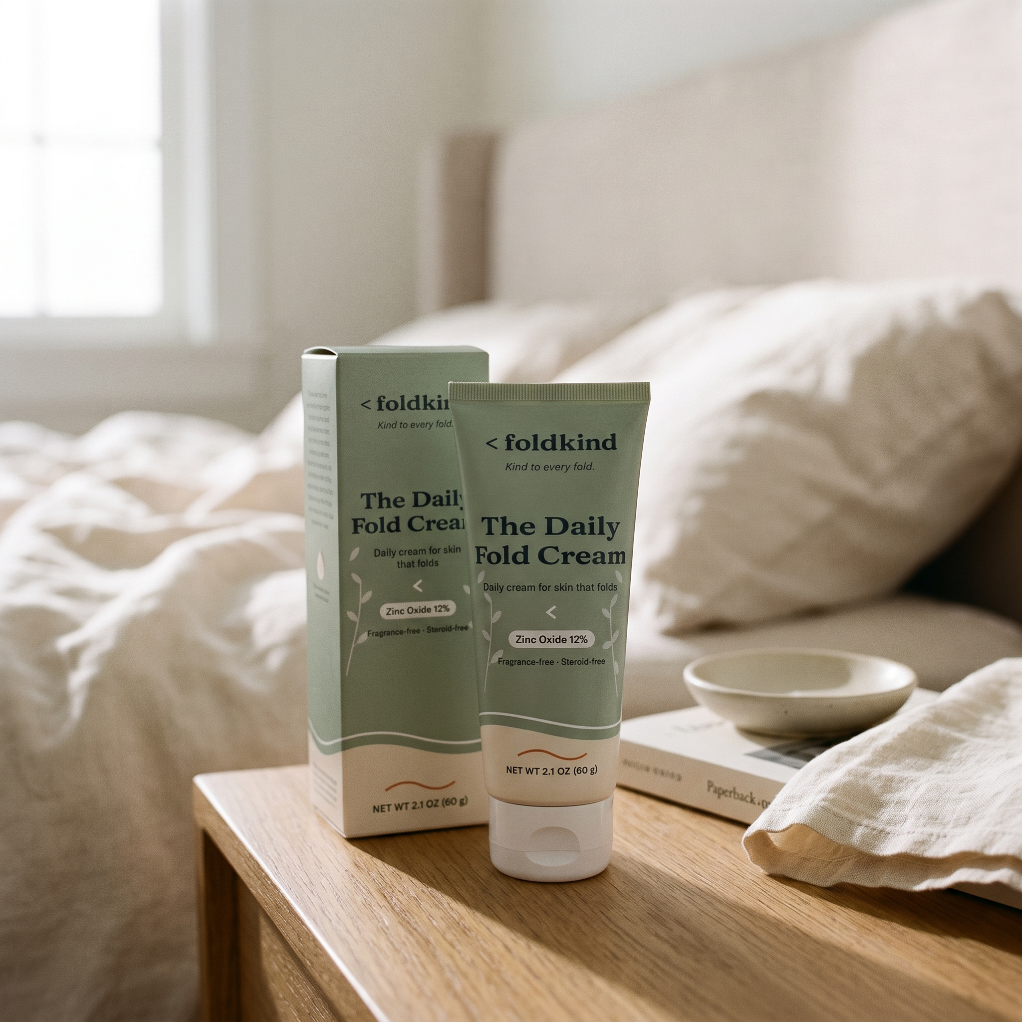 The Daily Fold Cream tube and its carton box on a bedside table in morning light, zinc oxide 12%, 2.1 oz (60 g), fragrance-free and steroid-free.