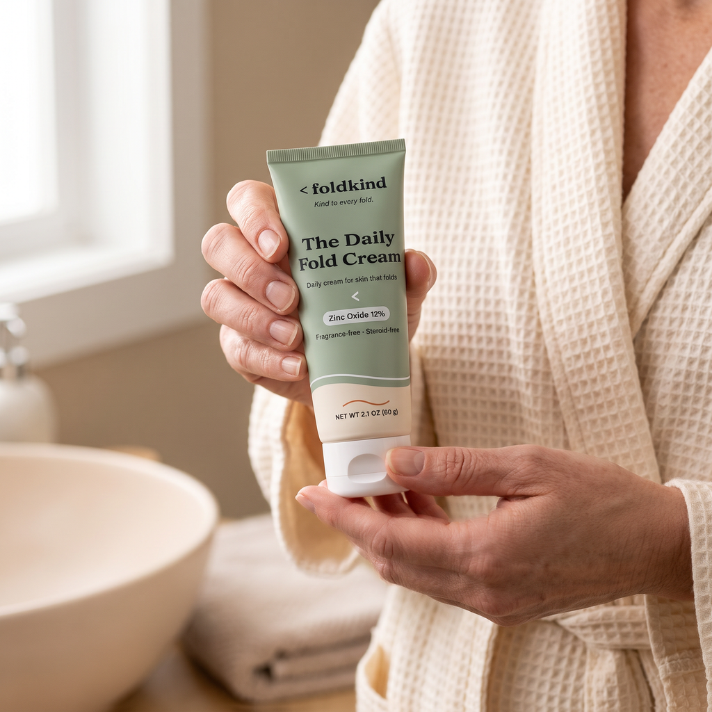 A woman in a bathrobe holding The Daily Fold Cream in her bathroom in morning light.